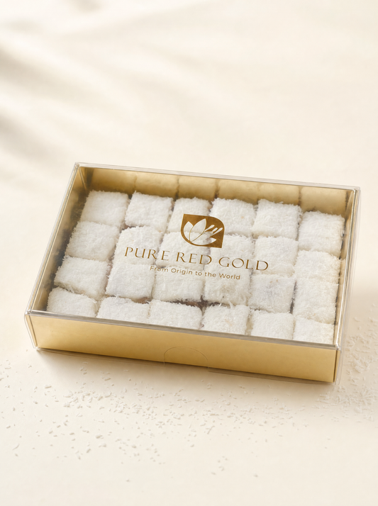 Gold gift box with a clear lid holding coconut-coated Signature Coconut delights, the PURE RED GOLD lockup printed in gold on the lid, on warm ivory