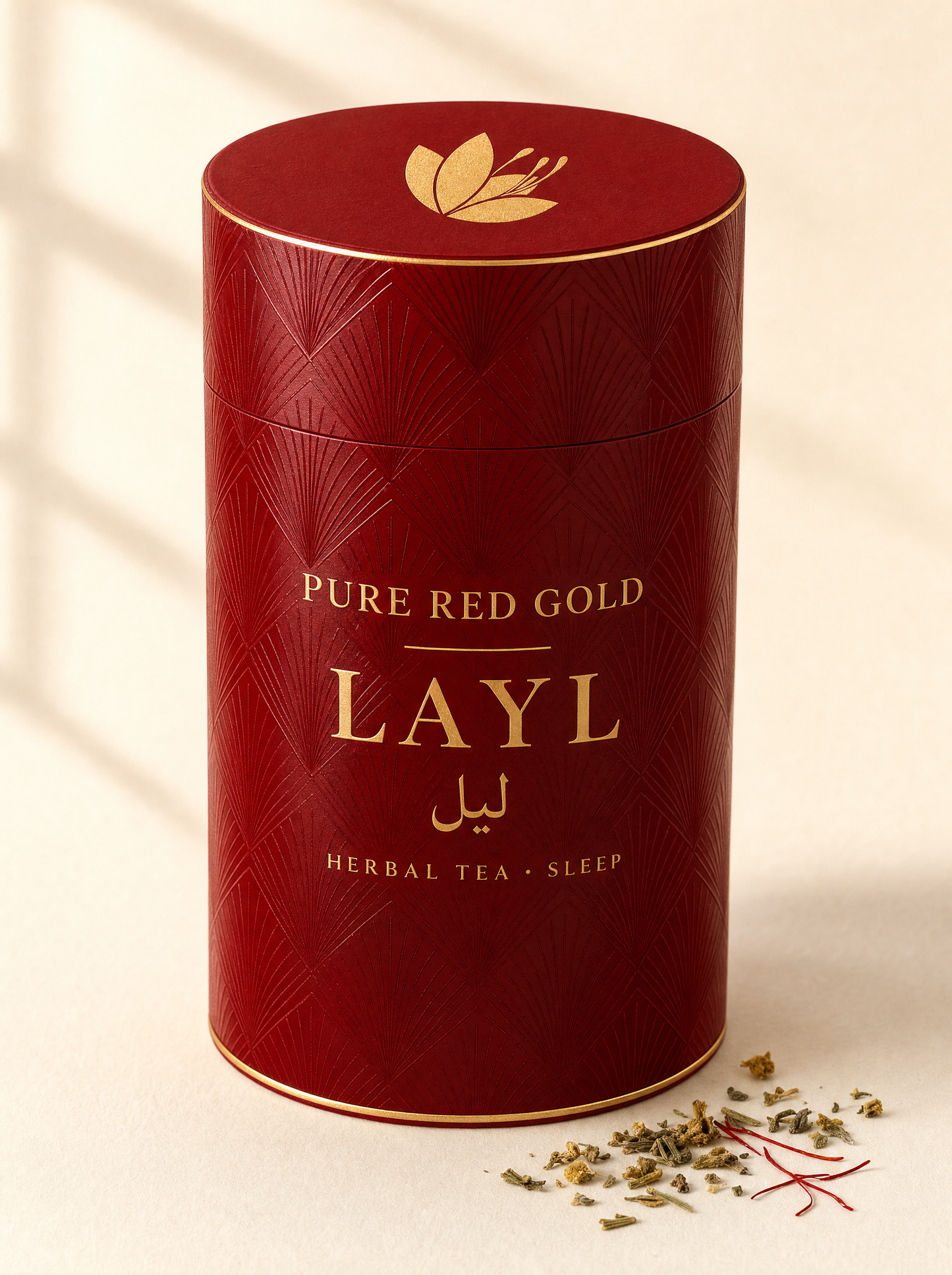 Layl herbal tea — a crimson cylinder tube with a tone-on-tone diamond and fan pattern, gold foil rims, the saffron crocus on the lid and LAYL with its Arabic name in gold foil, on warm ivory