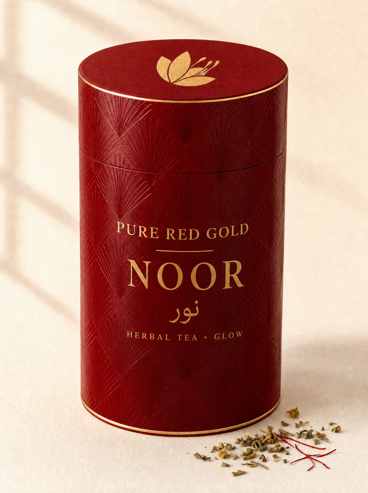 Noor herbal tea — a crimson cylinder tube with a tone-on-tone diamond and fan pattern, gold foil rims, the saffron crocus on the lid and NOOR with its Arabic name in gold foil, on warm ivory