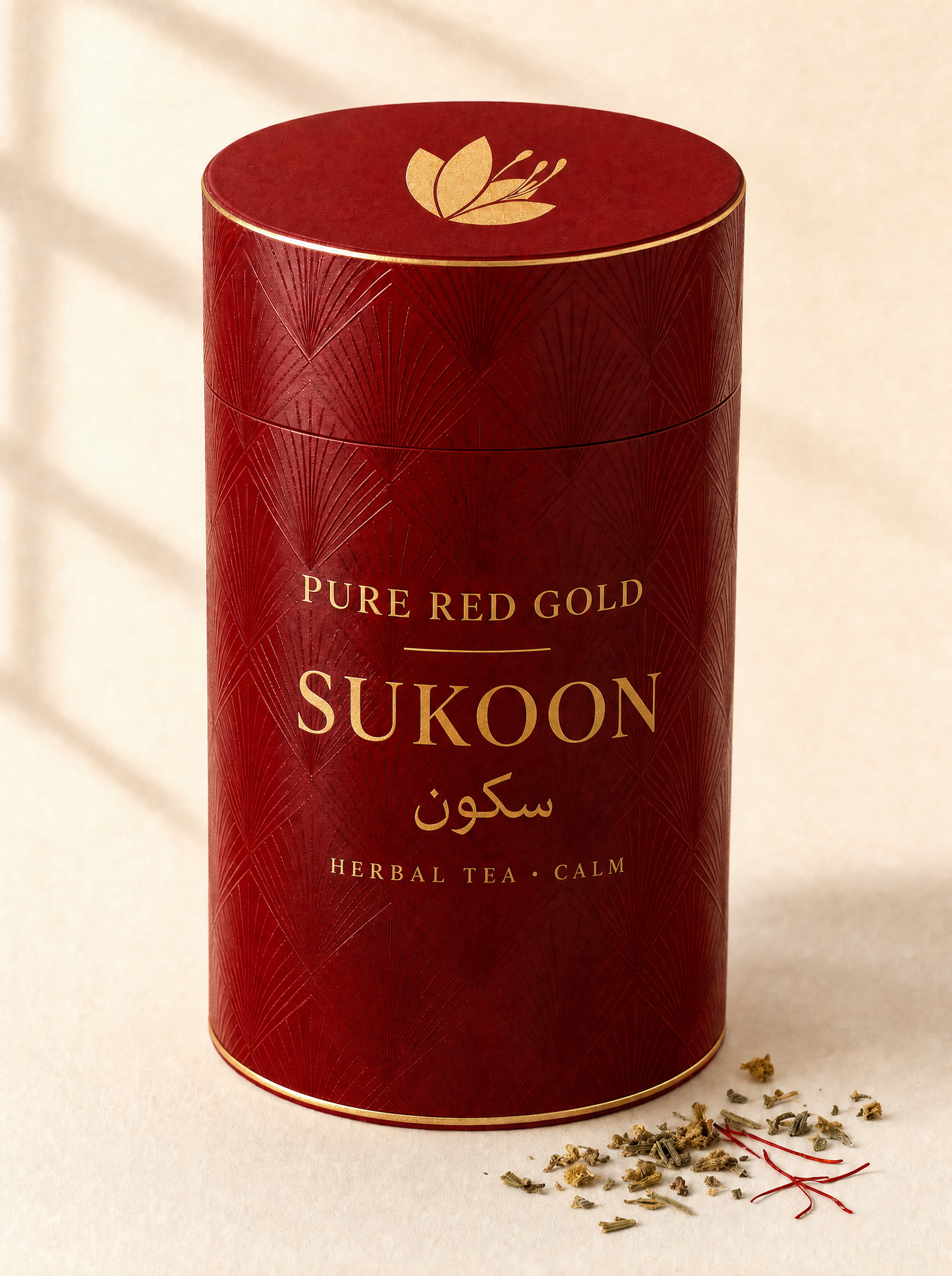 Sukoon herbal tea — a crimson cylinder tube with a tone-on-tone diamond and fan pattern, gold foil rims, the saffron crocus on the lid and SUKOON with its Arabic name in gold foil, on warm ivory