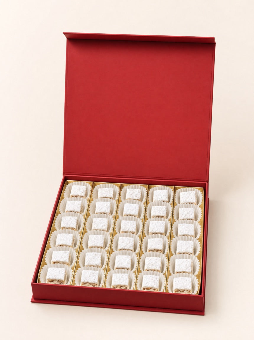 An open red Pure Red Gold gift box holding thirty coconut-rolled squares in fluted white paper cups, on warm ivory