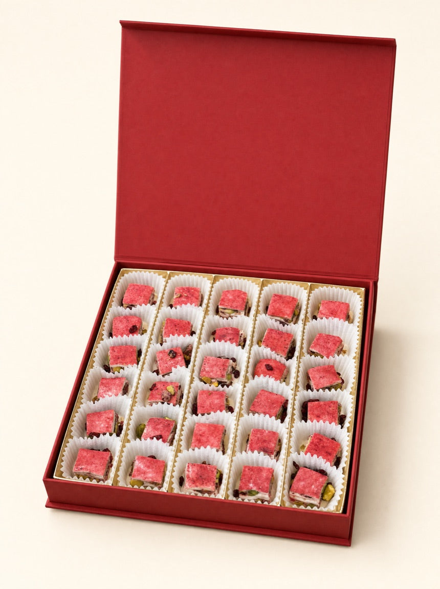 An open red Pure Red Gold gift box holding thirty barberry-dusted squares in fluted white paper cups, on warm ivory